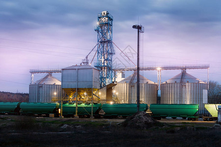现代钢制农业粮仓谷类储存仓库在夜间或日出时装载铁路货运车厢图片