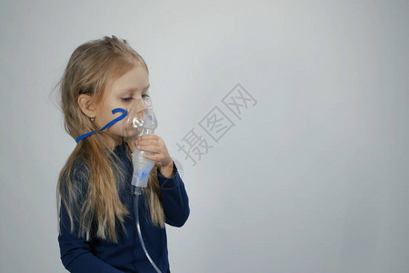 五岁的女孩在她的脸上戴雾化器的吸入面罩并呼吸使用雾化器图片