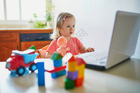 有膝上型计算机和玩具的愉快的蹒跚学步的女孩子使用电脑与朋友年长的亲戚或幼儿园的孩子交流孩子们的教育或在线交流背景图片