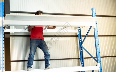 男手持木板准备在仓库或仓库中组装金属架图片