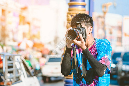 一名身着湿衣服的年轻摄影师用DSLR相机拍摄城市路上Songkran图片