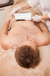 一名男客户用末层按摩器接受治疗师进行腹部按摩的垂直拍图片