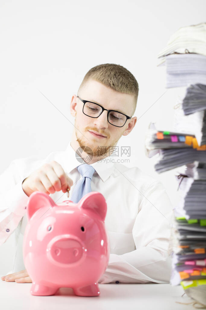 年轻严肃的男人把硬币放到办公室的粉红色存钱罐里图片
