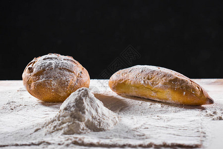 在面粉砂锅中的桌子特写上的新鲜面包厨房桌子上的新鲜面包健康饮食和传统面包店概背景图片