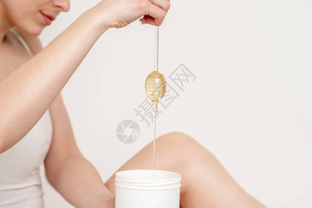 女人拿着蜂蜜棒同时将液体蜡流进白色背景图片