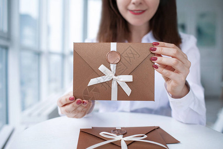 一张女手拿着带有蜡封礼券卡片婚礼邀请卡的青铜邀请信背景图片