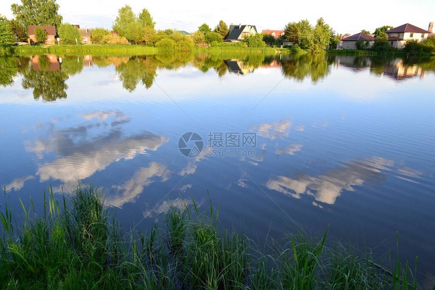 从湖到另一岸的村落以及水中天空和云层的反射景象在河边图片