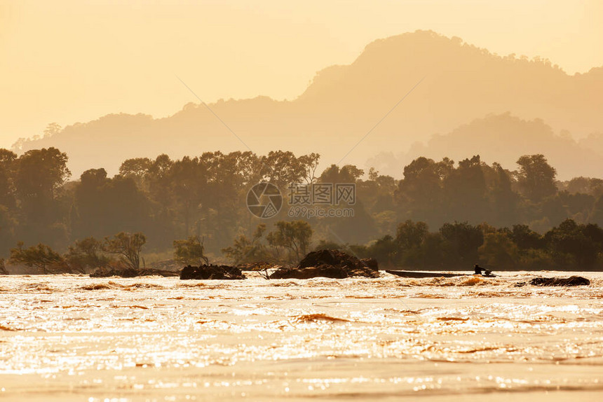 老挝渔民在黄昏的湄公河漂浮森林和背景山脉上驾驶一艘木船渡过快车图片