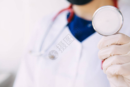身穿医疗大衣手套和面罩的年轻医生手握红色听诊器图片