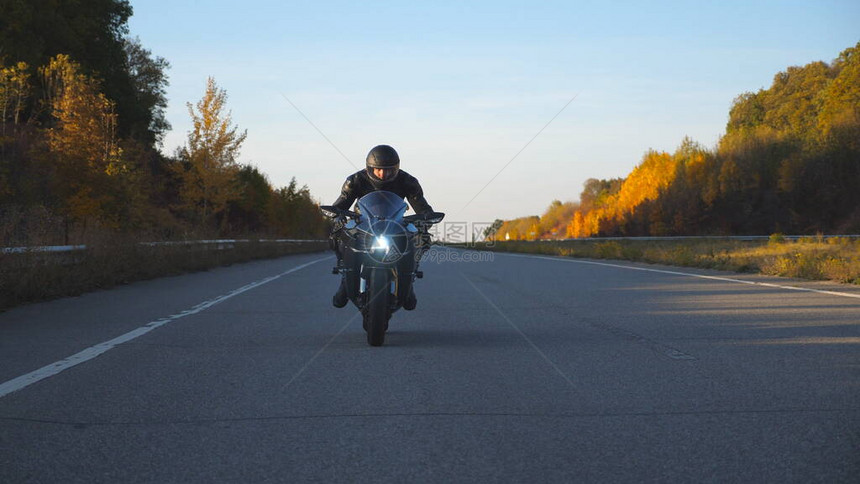 戴着头盔的男子在秋季公路上骑着摩托车摩托车手开着大灯在乡间小路上驾驶他的摩托车自由和旅行的概念慢动图片