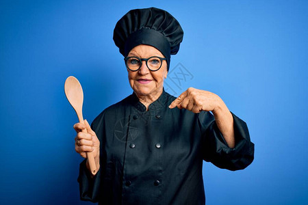 身穿炊具制服和帽子的灰发美女高级女厨师拿着木勺图片