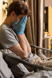 身戴医疗面罩在数字平板和拐杖旁边的床面遮盖着面部的残疾男子心图片