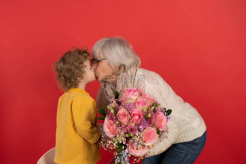 有卷发的小可爱男孩给他奶一束郁金香花红色背景假期和礼物的概念图片