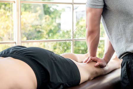 男治疗师向在体育物理治疗概念诊所床上的运动员病人提供腿部和小儿按摩图片