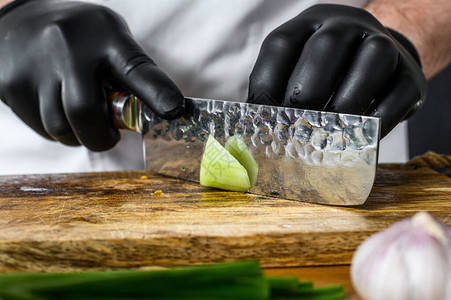 一个戴黑手套的厨师正在木制切削板上切开新鲜绿色图片