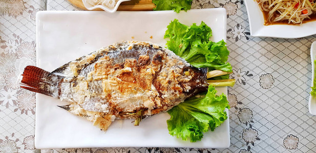 泰国餐厅的上放着绿卷心菜叶的盐烧罗非鱼这道菜是用泰国草药成分在食物中烤制而成的亚洲和健康的生活背景