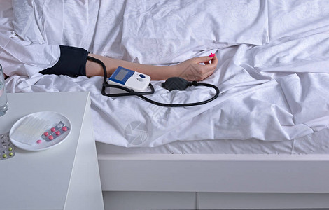床边桌子上有动脉血压和药物的生病妇女在床上睡觉图片