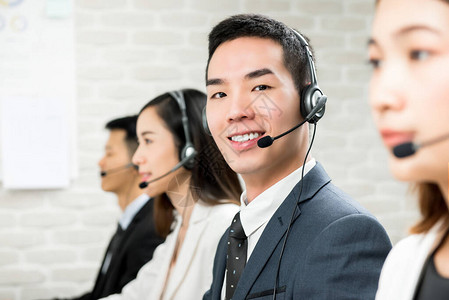 微笑的亚洲男客户服务电话销售代理在呼叫中心与团队一起工作的图片