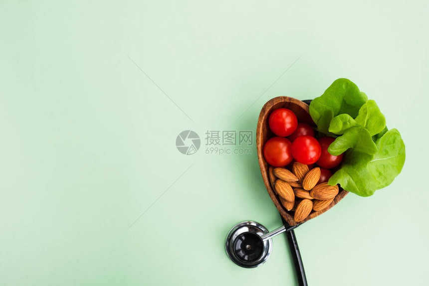 饮食药物和健康饮食对心脏的概念浅绿色背景上带有蔬菜和坚果的医用听诊器和盘子顶视图平图片