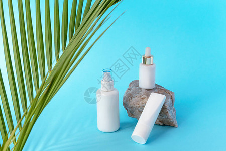 棕榈叶蓝色背景的空白包装中的化妆品提液奶油管和血清图片