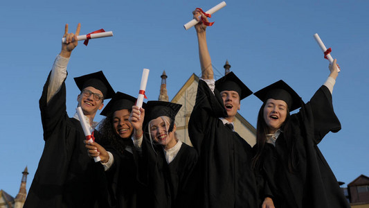 广角镜头慢动作终于自由了一群穿着毕业礼服和大师帽的快乐学生站在一起图片