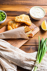 传统的炸鱼和薯条配豌豆泥塔酱客栈在木砧板上蘸皱巴的纸锥和柠檬图片