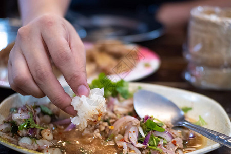 特写手指吃白盘中的糯米香辣猪肉沙拉图片