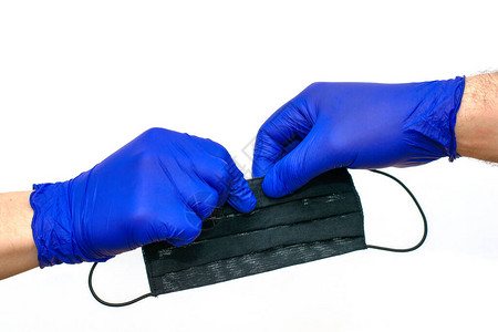戴蓝色医用防护手套的手将黑色医用口罩转移到白色背景上另一只图片