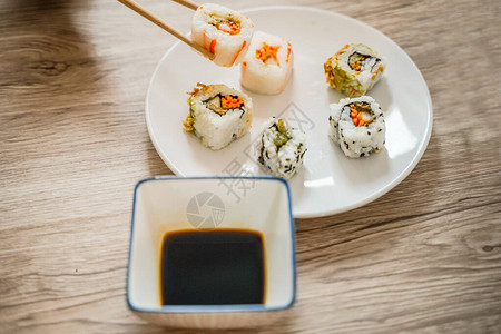 在木制餐桌上吃寿司卷使用筷子吃寿司卷图象的棍棒图片