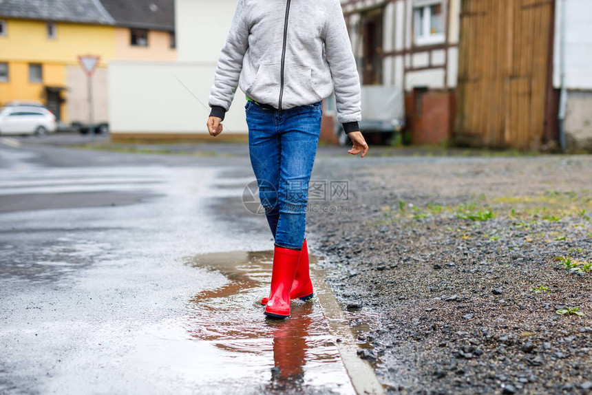 小男孩穿着红色雨靴在雨夹雪和雨天行走的特写镜头穿着五颜六色便服的孩子跳进水坑在户外玩乐图片