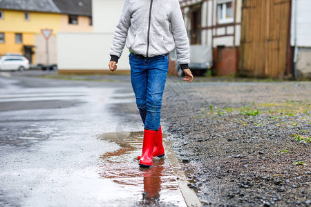 小男孩穿着红色雨靴在雨夹雪和雨天行走的特写镜头穿着五颜六色便服的孩子跳进水坑在户外玩乐背景图片