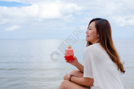 一个美丽的亚洲女人坐在海边喝西瓜图片