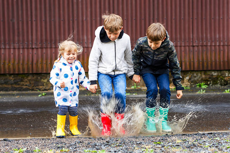 在雨夹雪中行走快乐的兄弟姐妹跳进水坑在户外玩得开心背景图片