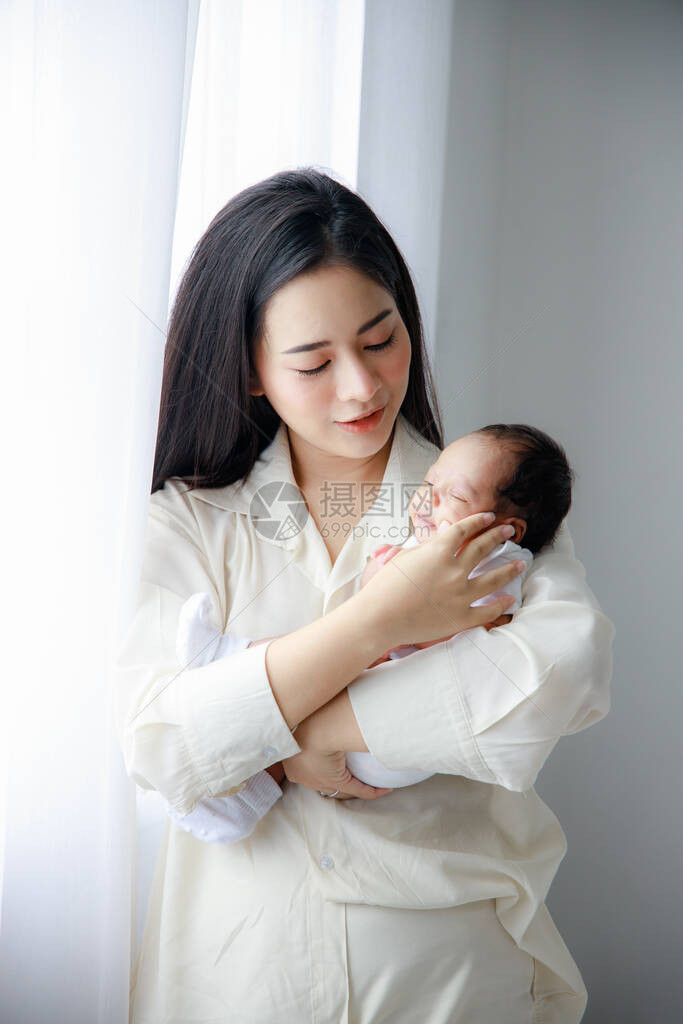亚洲年轻的母亲在白色的卧室里抱着一个刚出生的可爱婴儿妻子抚养孩子的义务母亲图片