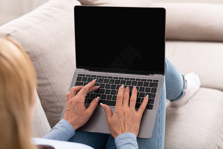 女人用空白屏幕打笔记本电脑坐在家里沙发图片