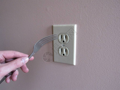 一个人将叉子插入墙上的电源插座图片