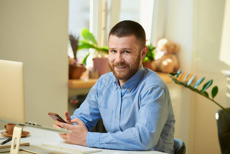 一个年轻人坐在笔记本电脑前的白色办公桌前摆姿势图片