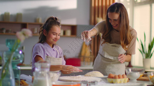 漂亮的女孩和妈在厨房里为饼干准备面团妈在家里的桌子上撒面粉女孩在家用厨房用面背景图片