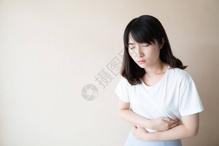 年轻的亚洲女在白色背景下因胃痛而受苦图片