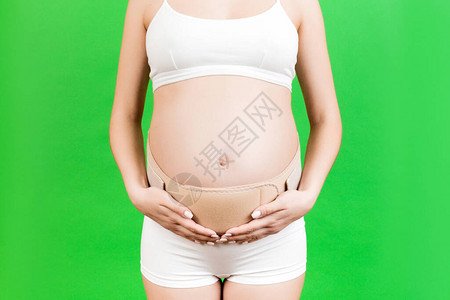 近身穿内裤的孕妇在绿色背景和复制空间使用孕带图片
