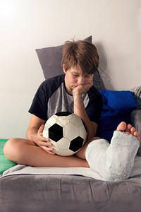 腿断了的无聊男孩坐在沙发上拿着足球断腿的男孩很无聊坐图片