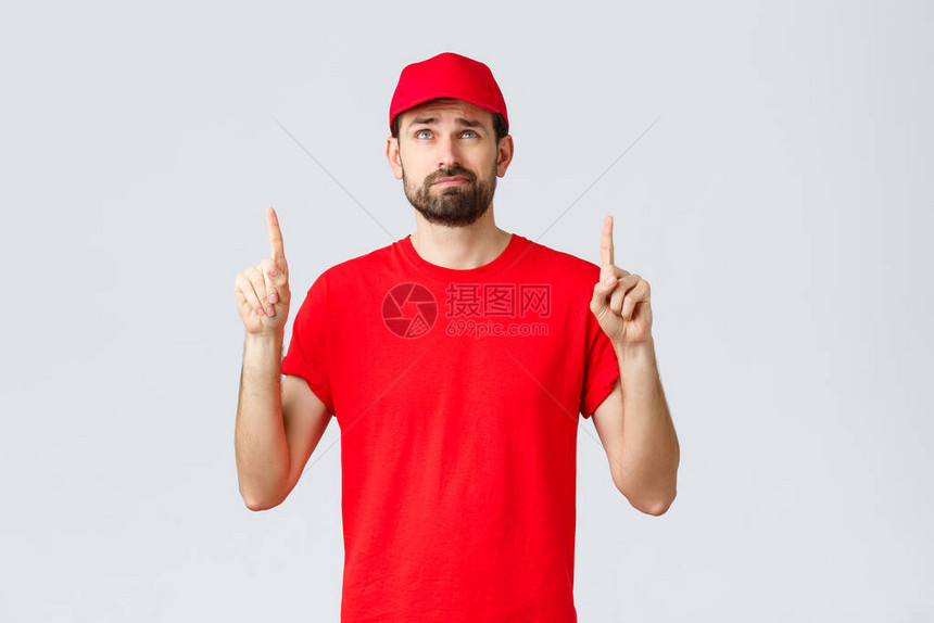 网上购物检疫期间的送货和外卖概念不高兴不情愿的年轻快递员穿着红色制服帽和T恤的员工图片