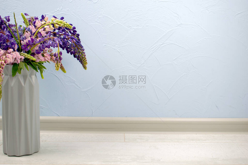 蓝色墙底或木地板上挂着紫花束和粉红色花朵的瓦塞图片