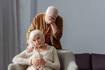 抑郁的老人站在生病的妻子身后图片