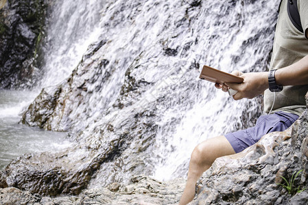 成年旅行男子使用智能手机站在瀑布附近独自旅行和积极的生活方式社会距图片