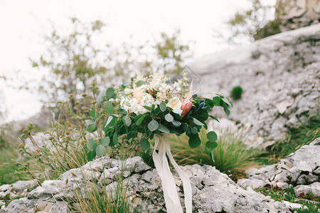 白色和奶油色玫瑰桉树枝普罗蒂亚刺飞燕草和岩石上的白色丝带的新娘花束图片
