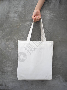 空白色手提袋帆布面料与手柄模拟设计女人手拿着生态或可重复使用的购物袋在垃圾灰色墙上的特写没有塑料袋和生态背景图片