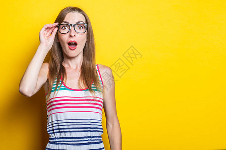 惊讶的年轻女孩拿着眼镜穿着黄色背图片