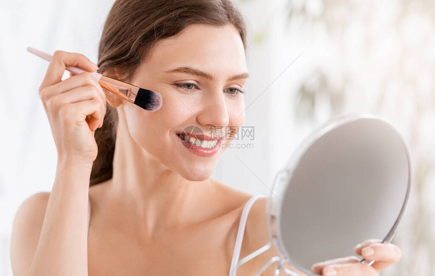 微笑的漂亮女人用刷子工具在脸上涂腮红图片