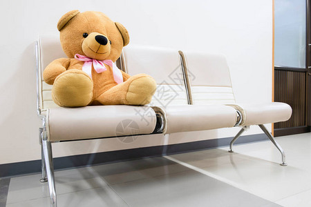 一只棕色泰迪熊坐在医院或诊所走廊等候区的椅子图片